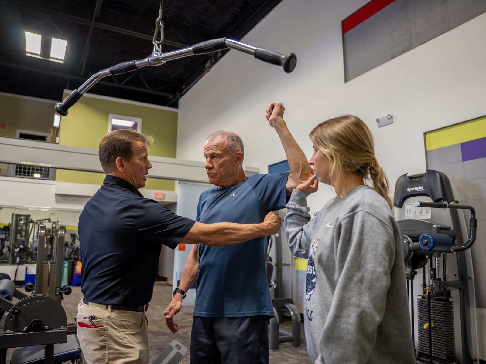 MCP – Personal Edge Fitness-35 Personal Trainer Educating an intern on muscles used during an exercise with an older man.